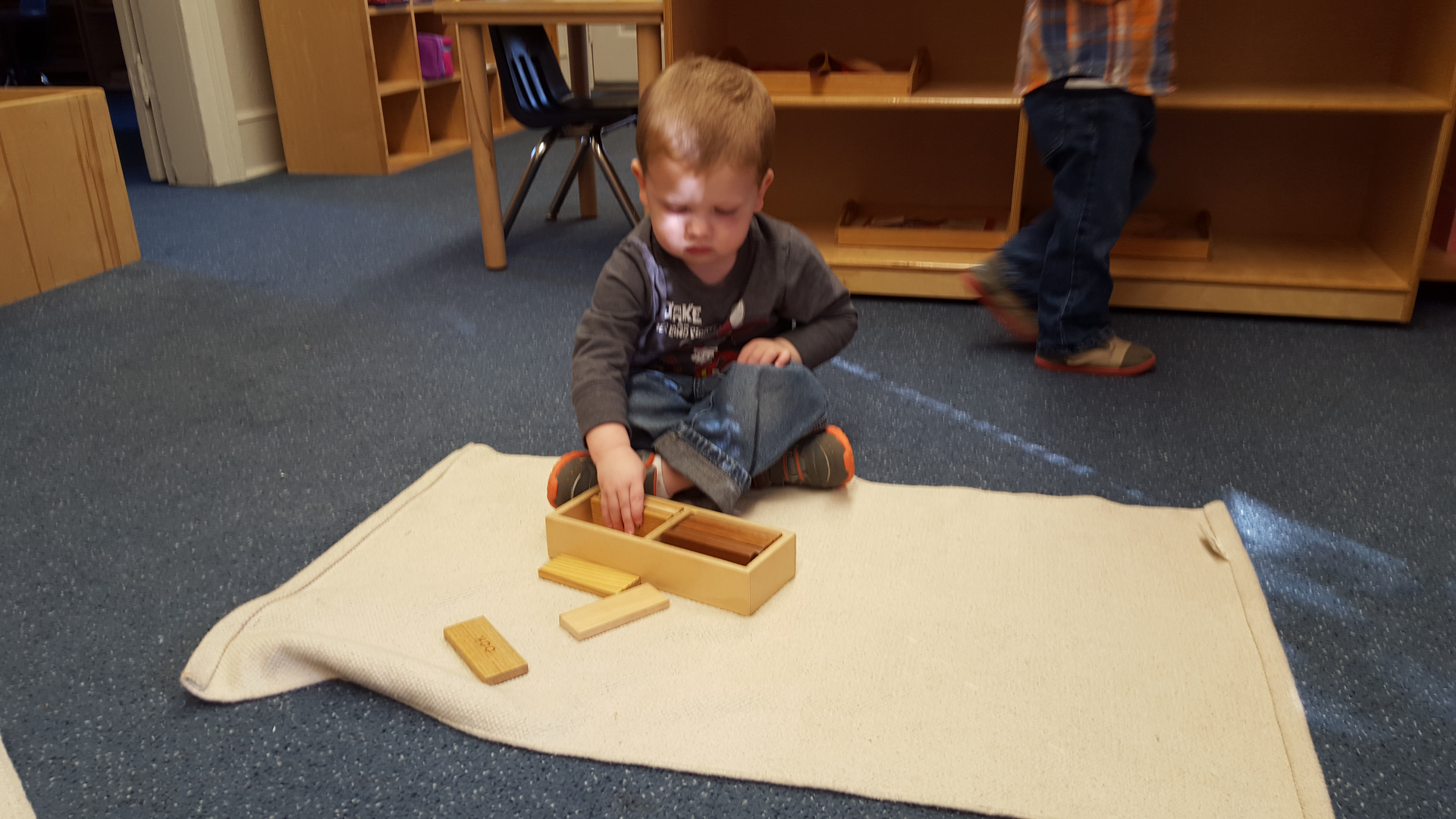 A boy working with a wooden box on a floor mat